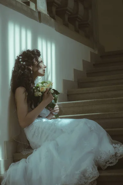 Gelin makyajı ve saç modeli ile kız. Düğün buketi şehvetli kadın. Çiçekli kadın merdiven üzerinde oturmak. Gelin moda beyaz elbiseli. Düğün ve gelecek bekliyor — Stok fotoğraf