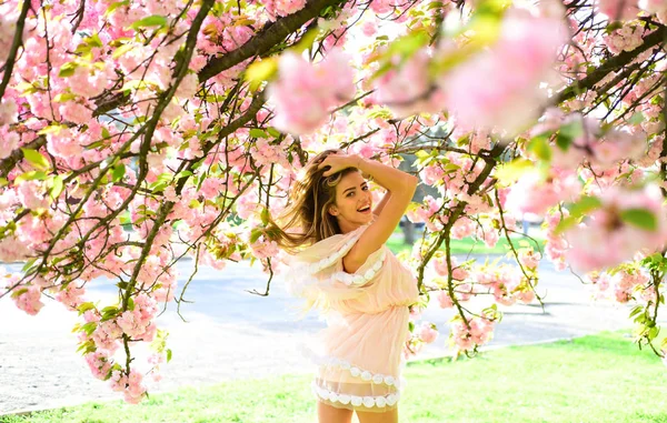 Blonde vrouw poseren onder kersenbloesem. Vrouw in mooie roze fladderende jurk wandelen in de botanische tuin. Gelukkig meisje speelt met haar lang blond haar, de schoonheid en de gezondheidszorg concept — Stockfoto