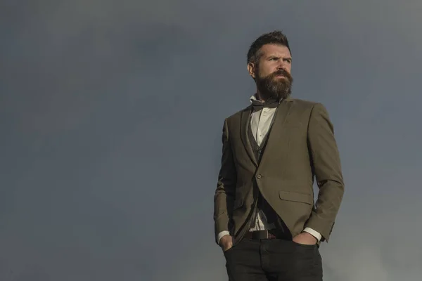 Hipster con barba e baffi sul viso non rasato. Uomo barbuto su cielo nuvoloso. Moda uomo d'affari indossare cappotto classico con papillon. Libertà e successo. Vacanze in viaggio e vagabondaggio, copiare spazio — Foto Stock