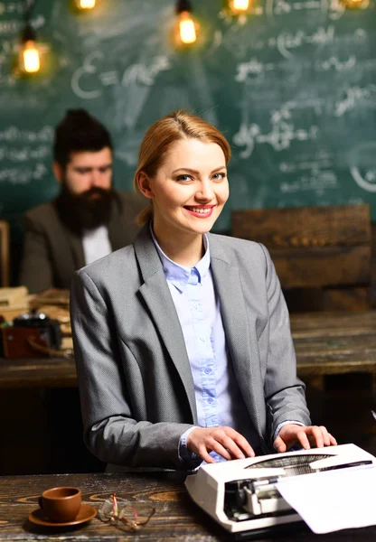 Buiness tipo de mujer en la máquina de escribir vintage con el hombre borroso en el fondo. Chica sensual mecanografía trabajo de investigación. Mujer feliz en traje de trabajo como máquina de escribir en la oficina. Belleza o moda y look — Foto de Stock