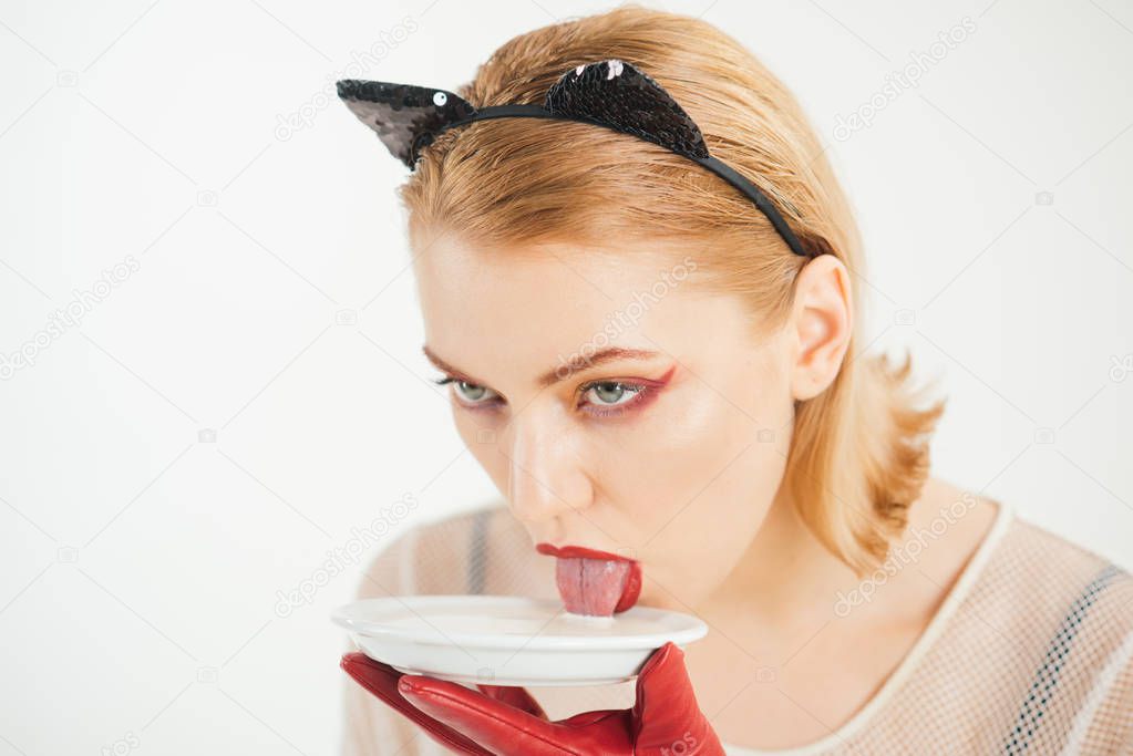 Girl in kitten ears and red gloves with yoghurt isolated on white. Dieting and health. Ecology product and heath. Cat woman eat sour cream. Sexy cat woman lick milk from plate. Food and drink.
