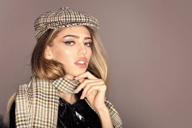 Seksi Bayan bahar, sonbahar kıyafeti. Moda aksesuarları kavramı. Kadın aksesuarları ile pelerin içinde sakin yüz. Uzun saçlı kız giyer ekose kepi, eşarp, gri arka plan, kopya alanı