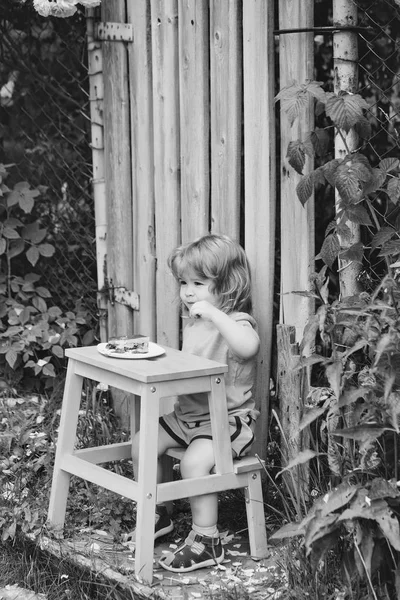 Kid enjoing his meal. small boy eating near rose bush — Stock Photo, Image