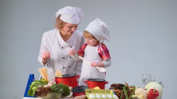 Lindo niño y su hermosa madre sonriendo mientras cocinaba en la cocina. Joven familia cocina comida en la cocina. Joven madre e hijo cocinando juntos . — Vídeos de Stock