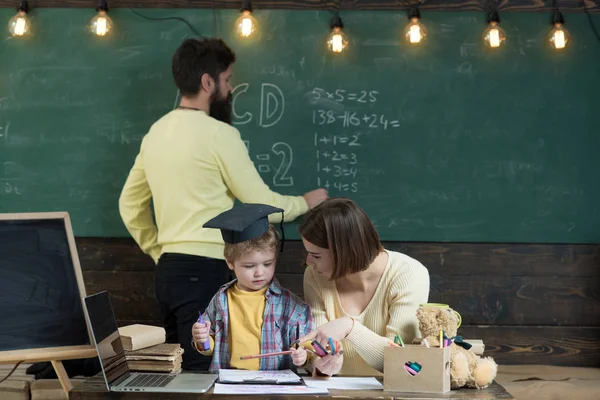 Matka uczy sprytny syna, podczas gdy ojciec zapisuje na tablicy na tle. Chłopiec słuchanie Mama z uwagą. Koncepcja domu. Rodzina troszczy się o edukacji ich synka smart — Zdjęcie stockowe