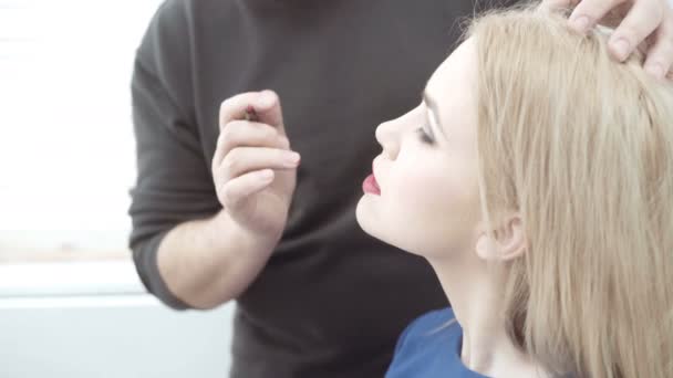 Maskérka aplikovat make-up na přitažlivou mladou ženou. Make-up pro mladé dívky. Mladá dívka v salonu krásy. Sexy blondýna v salonu krásy — Stock video