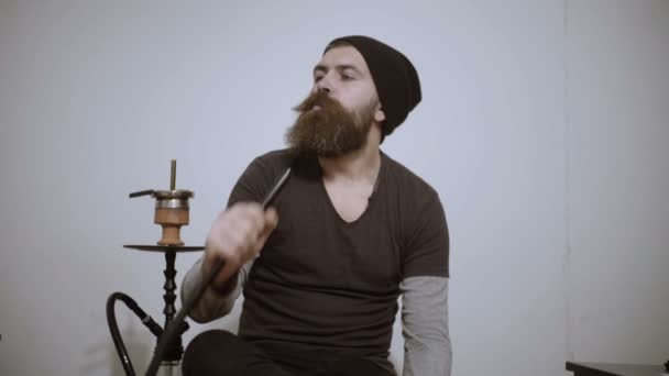 Young man smokes hookah and lets out smoke rings — Stock Video