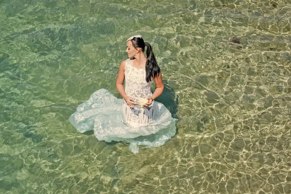 Huwelijksreis reizen concept. Mode en beauty. Meisje zit in zeewater. Bruid op zonnige zomerdag op zeegezicht — Stockfoto