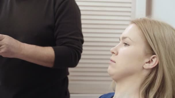 Maquilleuse appliquer le maquillage à une jeune femme attrayante. Maquillage pour jeune fille. Jeune fille dans un salon de beauté. Blonde sexy dans un salon de beauté — Video