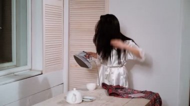 Güzel genç kadın giysileri Ütü, kameraya bakıyor ve dans