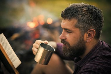 adam bir kitap okuma bir piknik. Adam gezgin okumak ve kamp ateşi alev içki