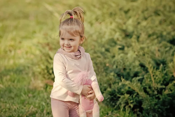 Alegria da criança. Menina feliz com sorriso de brinquedo macio no fundo natural — Fotografia de Stock
