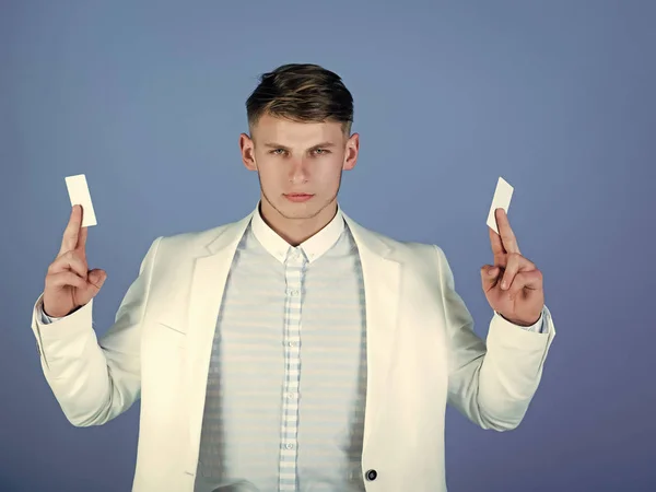 debit or credit card. Fashion and information concept. Banking and saving. Man holding business or bank cards. Businessman posing in white jacket and shirt. Manager wearing casual suit on blue
