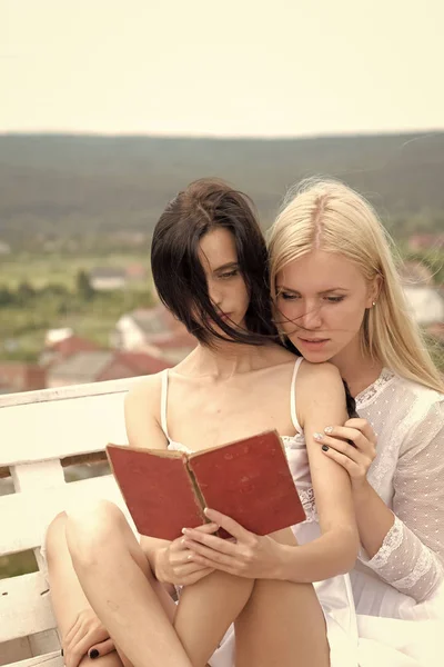 Flickor läser en bok. Kvinnor med blonda och brunett långt hår på landskap — Stockfoto
