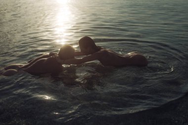 Bayan çıplak kalça ve gün batımında denizde yüzme sevgilisi ile ıslak. Maço ile çıplak kız yapar seviyorum. Balayı konsepti. Kaç arzu dolu denizde sarılmak. Aşık çift çıplak okyanus suda yüzmek
