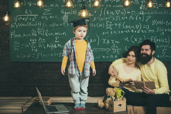 Smart child in graduate cap like to perform. Parents listening their son, checking mistakes with book chalkboard on background. Preparing for exam concept. Boy presenting his knowledge to mom and dad — Stock Photo, Image