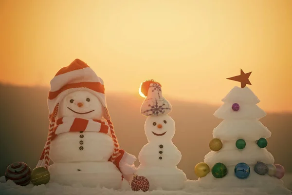 Concepto de celebración de vacaciones de invierno. Muñecos de nieve con caras sonrientes en sombreros en el paisaje nocturno — Foto de Stock