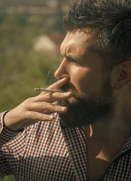 smoker. man smoking cigarette. young bearded hipster with beard and moustache on serious face smoking cigarette outdoor. unhealthy lifestyle and bad habit of guy with addiction. hairdresser and