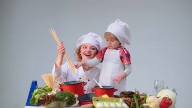 Sevimli küçük çocuk ve mutfakta yemek yaparken gülümseyen güzel annesi. Genç aile yemek yemek mutfakta. Çocuk çocukluk çocuklar mutluluk kavramı. Genç Anne ve oğlu birlikte yemek pişirme.