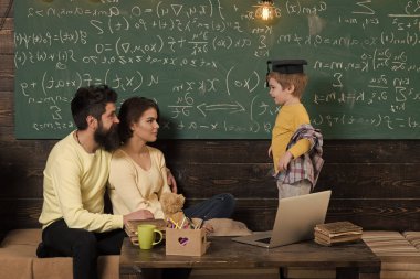 Evde eğitim kavramı. Lisansüstü şapkalı akıllı çocuk eğitim seviyor. Öğretim veliler evde çocuk. Çocuk Anne ve baba için onun bilgi sunma. Oğulları, kara tahta arka plan dinleme anne