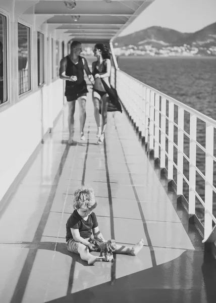 childish loneliness. Family travelling on cruise ship, defocused. Family rest concept. Father, mother walk on deck of cruise liner while kid playing with toy, landscape on background. Happy family on