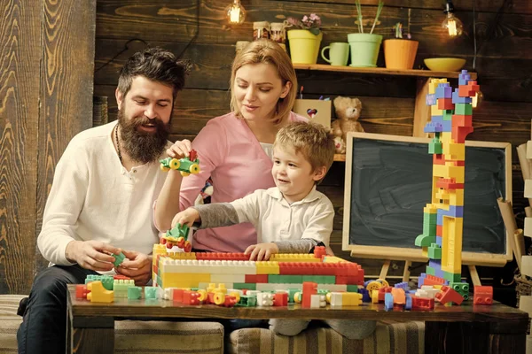 Cuidado de los padres. Madre e hijo lindo niño juegan con constructor. Concepto de tiempo familiar. Familia jugando con constructor en casa. Padre con barba ayuda a construir la pared de ladrillos de juguete, bloques de plástico . — Foto de Stock