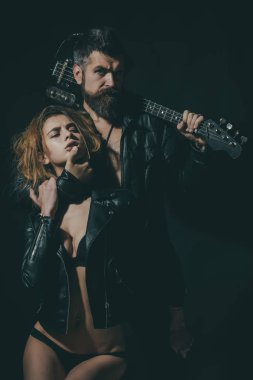 Rock and roll kavramı. Çift gitar, siyah arka plan ile sarılma aşık. Sakal ve seksi kız sutyen ile gitarist rock and roll yaşam tarzı tadını çıkarın. Çift seksi ve vahşi gitar ile poz