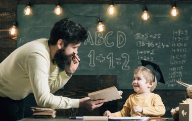 Harika çocuk ve dahi kavramı. Baba, öğretmen okuma kitabı, öğretim çocuk, evlat, kara tahta arka plan. Baba dahi oğlumu büyümek istiyor. Lisansüstü şapkalı çocuk çocuk dinleme babama seviyor