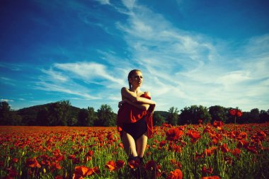 haşhaş tohumu alan. uzun kıvırcık saçlı kız siyah elbise yaz ve mavi gökyüzü arka plan, yaz, uyuşturucu ve sevgi zehirlenme, afyon yeşil kök ile kırmızı çiçek elbise