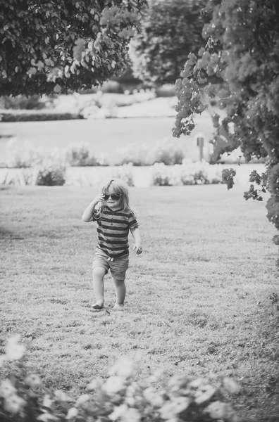 Mauvais garçon. enfant garçon sur marcher herbe dans des lunettes d'été près des fleurs — Photo