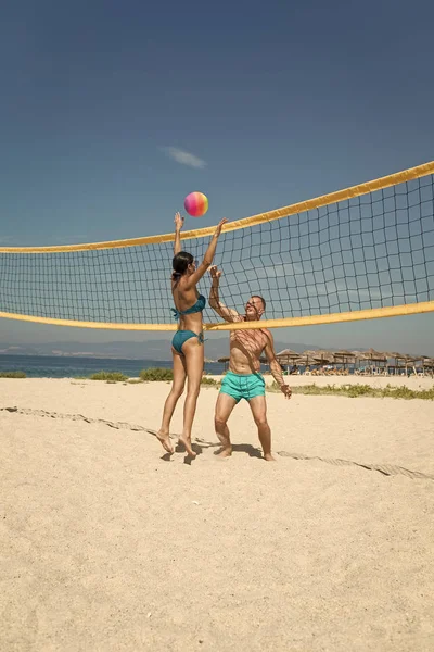 Beach volleyball concept. Couple have fun playing volleyball. Young sporty active couple beat off volley ball, play game on summer day. Woman and man fit, strong, healthy, doing sport on beach