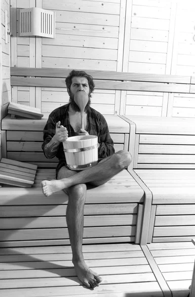 man in the sauna. handsome bearded man in wooden bath with bucket and spoon