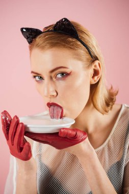 Kedi kadın ye ekşi krema. Ekoloji ürün ve heath. Diyet ve sağlık. Seksi kedi kadın yalamak süt plaka. Yiyecek ve içecek. Kız yavru kedi kulakları ve yoğurt pembe bir arka plan üzerinde kırmızı eldivenler.