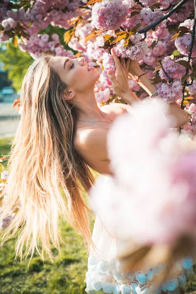 Mooie jonge vrouw genieten van zonnige dag in het park tijdens kersenbloesem seizoen op een mooie lentedag. — Stockfoto