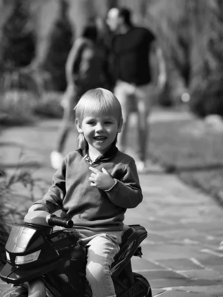 Niño alegre está descansando en el parque con sus padres. Niño feliz en bicicleta de juguete —  Fotos de Stock