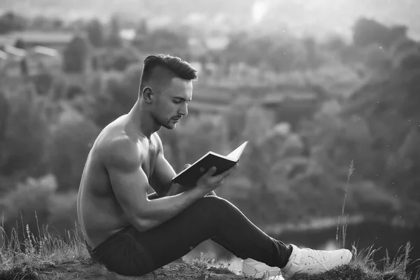 Ung kille läser en bok. Fundersam muskulös man med bok utomhus — Stockfoto