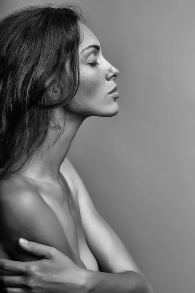섹시 한 관능적인 여자 나 예쁜 얼굴을 가진 여자와 벌 거 벗은 어깨와 가슴에 회색 배경, 근접 촬영으로 긴 갈색 곱슬 머리 — 스톡 사진