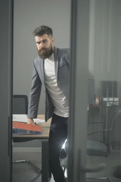 L'uomo barbuto guarda fuori dalla porta della stanza. Uomo d'affari in ufficio moderno con pareti in vetro. Uomo sicuro di se 'in giacca e cravatta sul posto di lavoro. Stile di vita aziendale e d'ufficio. Concetto di fiducia e successo — Foto Stock