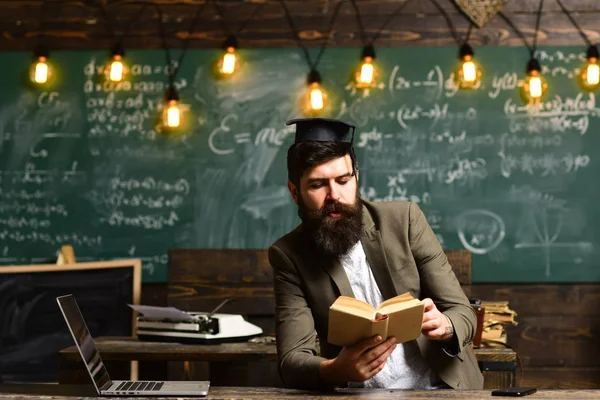 El barbudo leyó un libro en clase. Científico hipster con libro en pizarra. El hombre de negocios con traje lee en el escritorio de la escuela. Profesor con barba larga en cara de genio. Literatura en biblioteca y bibliopole —  Fotos de Stock