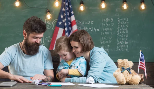 Parents teaching son american traditions playing. Kid with parents in classroom with usa flag, chalkboard on background. American family sit at desk with son and usa flag. Patriotic education concept — Stock Photo, Image