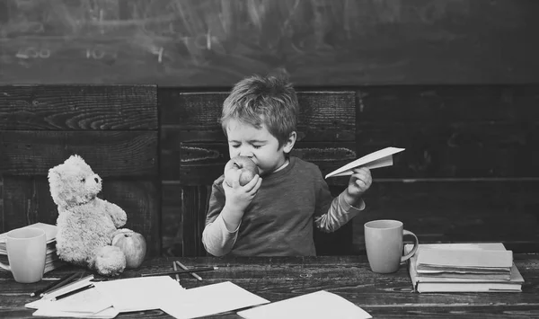 Pause entre les cours. Enfant mangeant des pommes avec plaisir. Mignon garçon mordant des fruits avec les yeux fermés. Nourrisson jouant avec un avion en papier — Photo