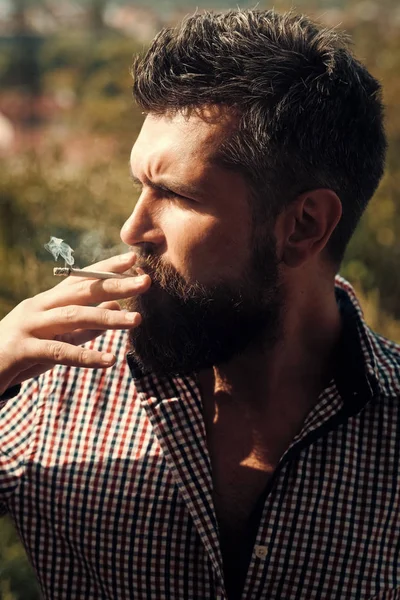 Hombre fumando cigarrillo. joven barbudo hipster con barba y bigote en la cara seria fumar cigarrillos al aire libre. hombre fumando cigarrillo. estilo de vida poco saludable y mal hábito de chico con adicción — Foto de Stock