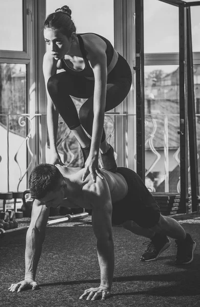 Concepto de deporte y gimnasio. Hombre y mujer en ropa deportiva en el gimnasio, ventana en el fondo. Pareja hace acroyoga, práctica física de yoga y acrobacias. Atletas musculosos y fuertes practicando acroyoga en el gimnasio — Foto de Stock