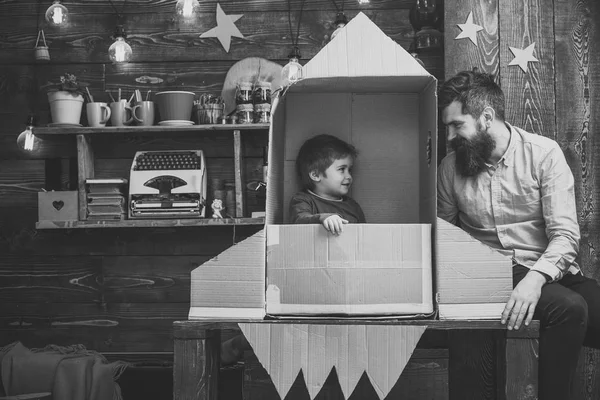 Niño lindo chico jugar cosmonauta, astronauta. Niño feliz sentarse en cartón hecho a mano cohete. Chico jugar con papá, padre, pequeño cosmonauta sentarse en cohete hecho de caja de cartón. Concepto de lanzamiento de cohetes —  Fotos de Stock