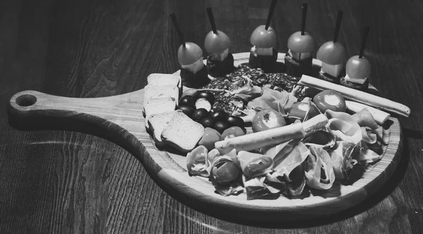 Koude snacks. Bord met hapjes op houten tafel. Snacks smakelijk geserveerd op ronde bord. Schotel restaurantconcept. Koude voorgerechten met tomaten, worst, salami, ham, rucola, olijven en brood — Stockfoto