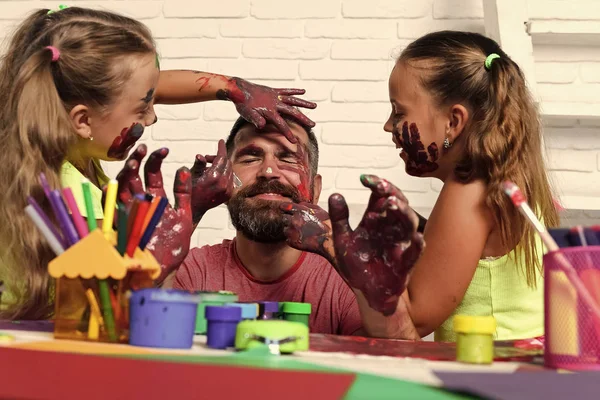 Děti se bavit s jejich otcem. Dívky na člověka čelí kůži s barevnými laky — Stock fotografie