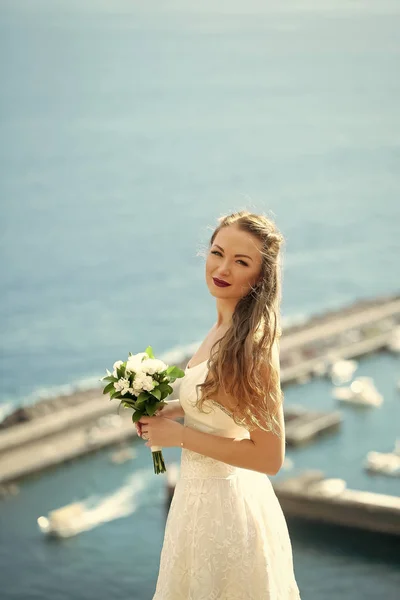 Noiva bonita, mulher sexy em vestido branco com casamento bouquet fica no topo da montanha em idílico, ensolarado, dia de verão . — Fotografia de Stock