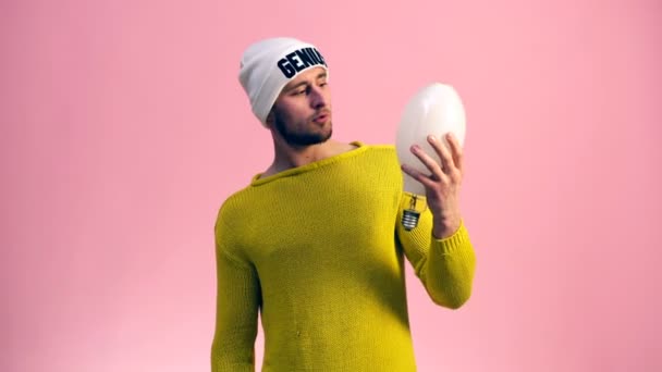 Ein Mann im gelben Pullover blickt auf eine große weiße Lampe auf rosa Hintergrund. Genie. Idee. Erfindung. Entdeckung — Stockvideo