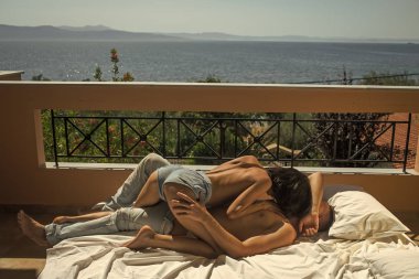 Seksi çift. Adam ve aşk seksi üstsüz kadın yapar. İki aşk hugs ve balkon, arka plan Denizde öpüşme sonra. Çift beyaz sayfalarda yatıyordu, güneşli günde terasta seks. Seks ve balayı