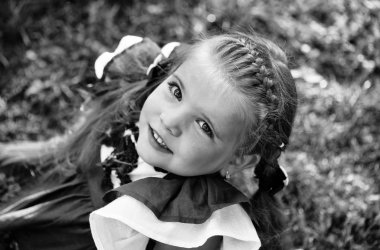 mutlu birinci sınıftan. Mutlu sevimli kız örgü saçlı yeşil çimenlerin üzerinde gülümseyen